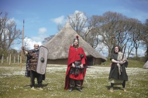 People in Roman costume posing in front of a celtic rooundhouse