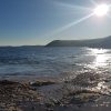 View across a beach on a sunny day with a view across the shallows to a headland jutting out into the sea in the distance. Location pictured is Manorbier, Pembrokeshire