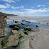 View across a rockpool on a sandy beach on a sunny day with a headland jutting into the sea in the background. Location Pictured is Newgale, Pembrokeshire