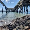 View from beneath a pier structure jutting out into a body of water with pipes running along one side of the structure. location is South Hook, Pembrokeshire