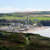 View of a small seaside town next to a sandy beach surrounded by grassy fields. The beach is busy with people enjoying a sunny day