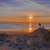 The sun setting above a sandy beach creating an orange glow across the sky and sea. In the foreground a pile of pebbles has been added to small sand dune mound with a small crucifix as its top. This is to mark the apparent site of Dobby&#039;s Grave, a fictional character from the Harry Potter books.