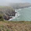 Photograph of limestone cliffs topped with grass on a misty day with bluegreen seas crashing against the bottom of the cliffs.