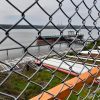 View of a ship docked at an industrial facility, photograph taken through a chain link fence.