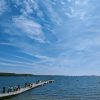 People walking along a floating pontoon where a number of small boats are moored and one larger boat awaits them. The pontoon is extending out into a relatively calm sea on a sunny day with blue skies and wispy clouds. In the distance you can see a number of boats moored out int the bay. Location pictured is Dale, Pembrokeshire