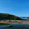 Several boats moored in a tidal harbour at low tide, leaving many of them leaning as the tide recedes leaving a sandy bed below.  It&#039;s a sunny day with clear blue skies. Location pictured is Solva, Pembrokeshire