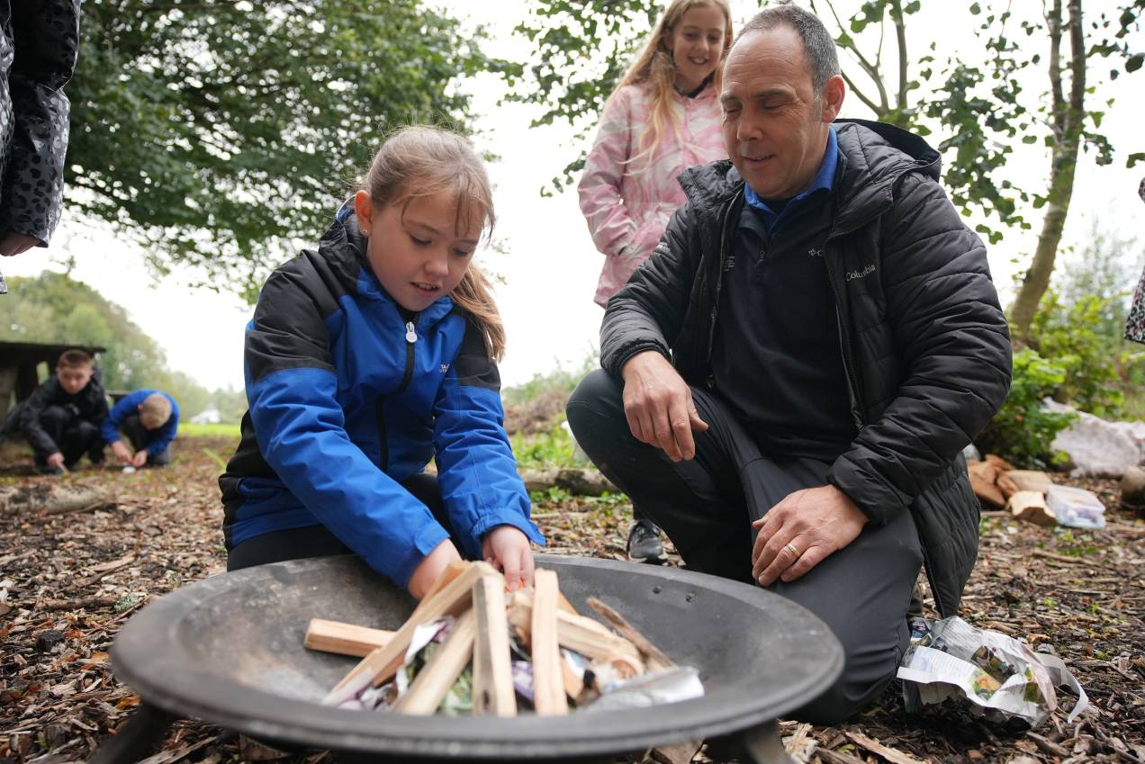 A young girl learning how to light an outdoor fire with the help of PODS staff