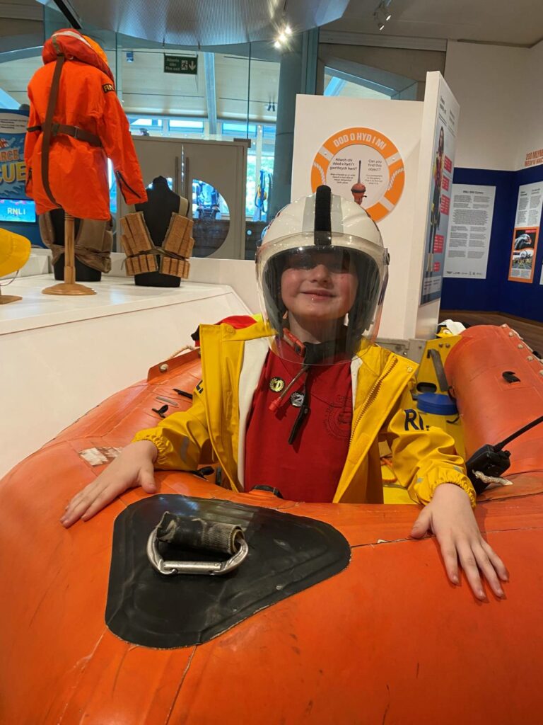 A young boy sitting in the Arancia lifeboat, wearing RNLI gear, including a helmet.